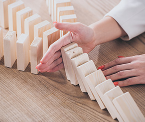 Hand protecting falling dominos, symbolizing risk mitigation and safeguarding organizations from cascading security threats.